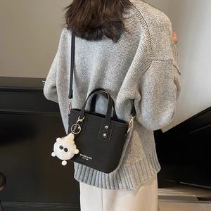 Chic black bucket bag with plush charm, styled over the shoulder on a grey knit sweater