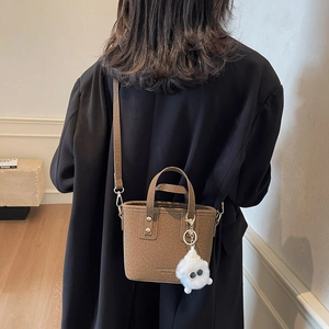 Brown felt bucket bag with shoulder strap and white plush charm on model in black coat