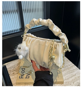 Close-up of cream pleated handbag with gold chain strap and soft ruched handle detail