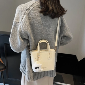 Chic cream-white bucket bag with plush charm and crossbody strap on a grey sweater model