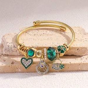 Detailed shot of a gold beaded bangle with green gemstone and heart charm on stone