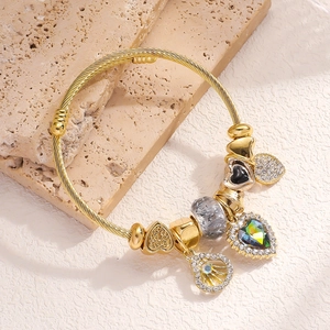Close-up of gold woven bangle featuring crystal heart and black enamel charms on stone