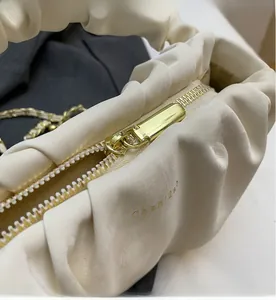 Close-up of smooth gold zipper and soft pleated texture on beige crossbody bag