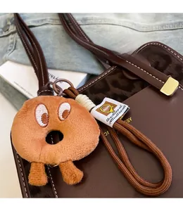 Close-up of a plush doughnut bag charm with embroidered eyes on a leather tote