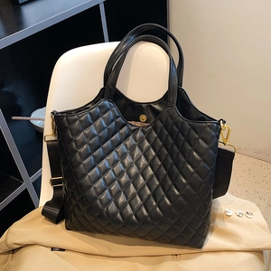 Black quilted diamond tote bag with wide strap and gold hardware on a stylish trench coat