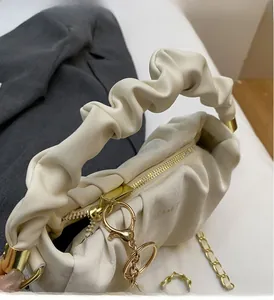 Detail of beige pleated cloud bag with scrunchie handle and gold chain hardware accents