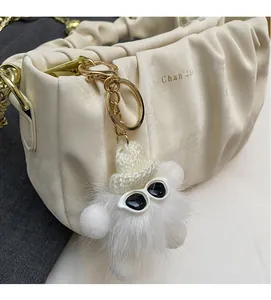 Close-up of white plush monster keychain with sunglasses and hat on a beige bag