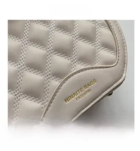 Détail du sac bandoulière matelassé beige avec logo doré et finitions de couture