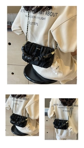 Detail of black pleated bag with gold chain strap and a white plush toy charm