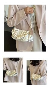 Detail of off-white pleated cloud bag with gold chain strap and plush pendant decor