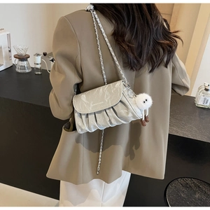 Détail du sac argenté plissé avec chaîne en métal et breloque en forme de poupée en peluche