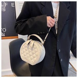 Détail du sac bandoulière rond blanc matelassé avec chaîne dorée porté par un mannequin
