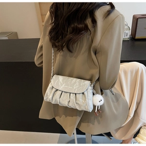 Détail d'un sac à bandoulière gris plissé avec chaîne en métal et pompon blanc en peluche