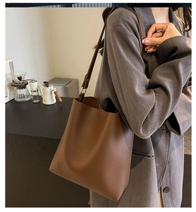 Detail of brown lychee grain leather bucket bag with slim shoulder strap on a model