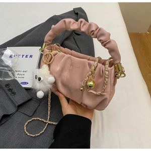 Detail of pink pleated handbag with gold chain strap and fluffy charm on a blazer