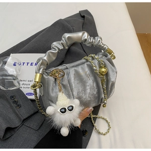 Detail of silver pleated cloud bag with golden chain and plush doll on a blazer