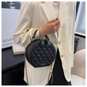 Sac rond matelassé noir avec chaîne dorée, porté sur une veste de blazer blanc