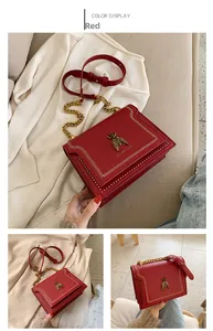 Detail of red crossbody bag with golden bee emblem and elegant metal chain strap