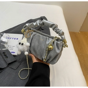 Detail of silver pleated handbag with metallic finish, gold chain, and white plush charm