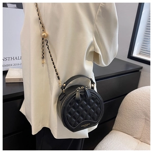 Détail d'un sac rond matelassé avec chaîne dorée et poignée porté sur un blazer blanc