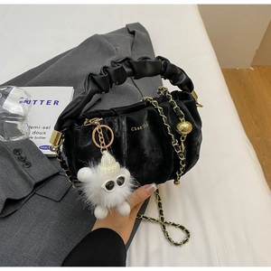 Detailed view of black pleated cloud bag with gold chain and furry pompom charm