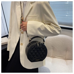 Détail du sac rond noir matelassé avec chaîne dorée porté sur un costume blanc