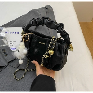 Detail of black pleated cloud bag with gold chain and white plush charm on a table
