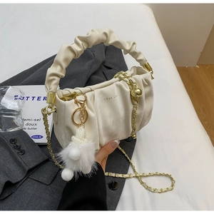 Detail of a creamy white pleated handbag featuring a ruffle handle and gold chain strap
