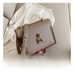 Close-up of a taupe leather handbag with a golden bee metallic emblem and chain strap
