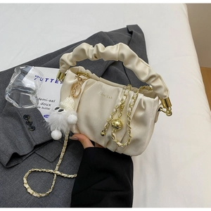 Close-up of ruched cream handbag with gold chain strap and plush pendant detail
