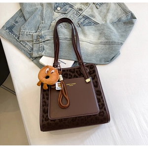 Detail of leopard print tote bag featuring brown leather trim and cute plush charm