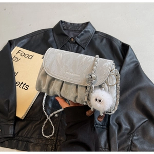 Détail du sac plissé gris clair avec chaîne argentée et breloque en peluche sur du cuir