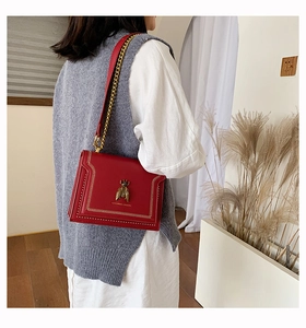 Detail of red crossbody bag with vintage gold bee clasp and white V-shaped stitching