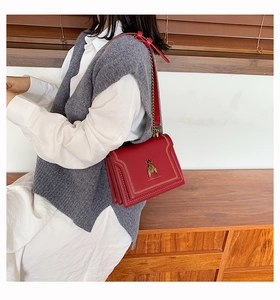 Detailed view of red crossbody bag featuring gold bee hardware and chain strap on model