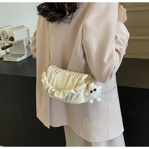 Detail of white pleated cloud bag with gold chain and plush monster charm on model