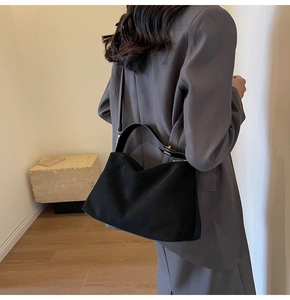 Detail of a matte black minimalist shoulder bag styled with a gray blazer for a chic look