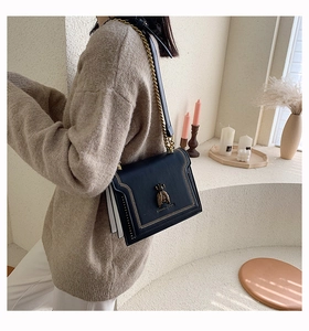 Detail of vintage black shoulder bag featuring gold bee buckle and V-shaped stitching