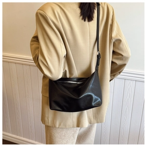 Detail of a minimalist black leather crossbody bag with silver hardware on a model