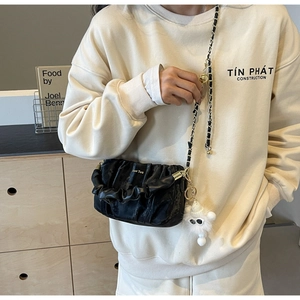Close-up of black pleated cloud bag with gold chain strap and white plush charm accessory
