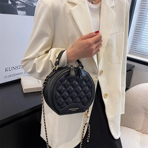 Petit sac rond noir matelassé avec bandoulière chaîne dorée porté sur un blazer
