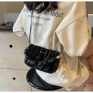 Detail of black pleated crossbody bag with gold logo, chain strap and white cat plush charm