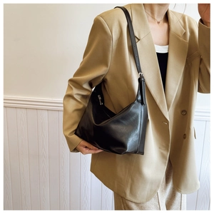 Detail of minimalist black leather hobo bag worn by a model in a light khaki suit