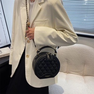 Petit sac rond noir matelassé avec bandoulière en chaîne porté sur un blazer blanc