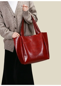 Detail of red oversized leather tote bag showing glossy texture and wide shoulder strap