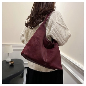 Detail of burgundy matte leather hobo bag with contrast stitching on model shoulder