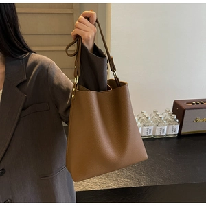 Detail of lychee pattern leather and gold hardware on brown bucket bag with straps