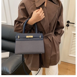 Detail of dark blue trapezoid handbag with gold metal clasp on a stylish brown coat