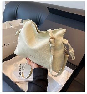Détail du sac seau en cuir crème avec cordon et nœud décoratif dans une boîte cadeau