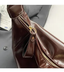 Détail de la fermeture éclair dorée et du cuir brillant marron foncé du sac cabas