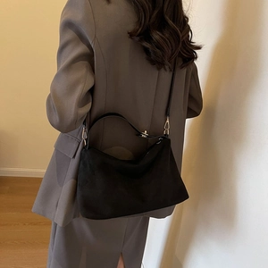 Minimalist black suede underarm tote bag with gold hardware shown on a model